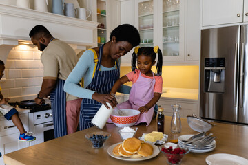 African american mother and daughter mixing batter in bowl while father and son making pancakes
