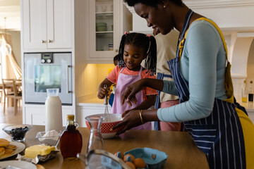 African american mother and daughter mixing batter with whisk in bowl on table in kitchen