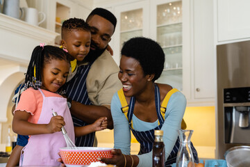 Happy african american parents and children mixing batter in bowl on table in kitchen