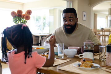 African american father talking with daughter while having breakfast at dining table at home