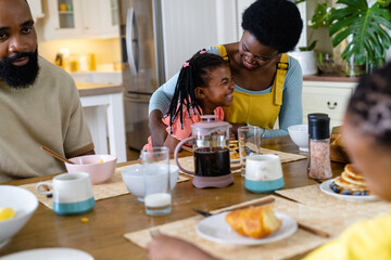 Fototapeta na wymiar African american mother and father having breakfast with cheerful daughter at dining table