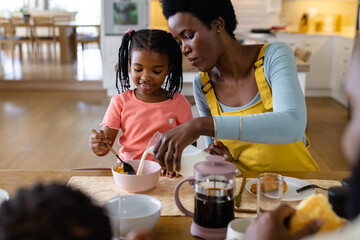 African american mother pouring milk in breakfast cereals for daughter at dining table at home