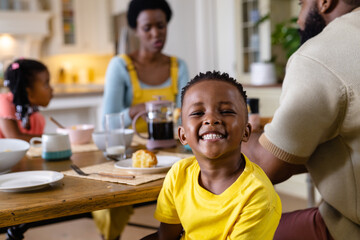 African american boy smiling and looking at camera while having breakfast with family at table