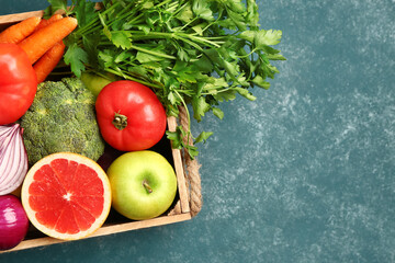 Wooden box with different fresh fruits and vegetables on green background, closeup