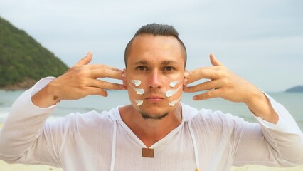 Close-up portrait man apply sun cream protection lotion, looking at camera.Stylish man on beach...