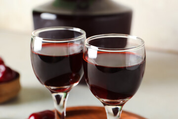 Glasses and bottle with sweet cherry liqueur on white background, closeup