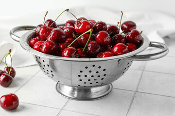 Colander with sweet cherries on white tile table