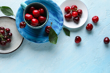 Cup and plates with sweet cherries on blue background