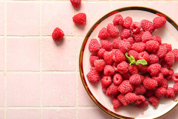 Plate with fresh raspberries and mint on pink tile background
