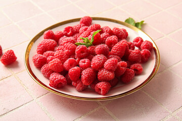 Plate with fresh raspberries and mint on pink tile background