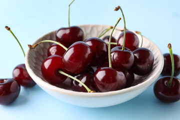 Bowl with sweet cherries on blue background
