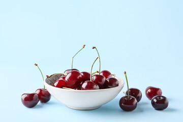 Bowl with sweet cherries on blue background
