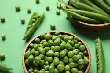 Bowls with fresh green peas on color background