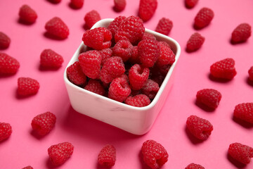 Bowl with fresh raspberries on pink background