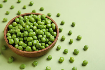 Bowl with fresh green peas on color background