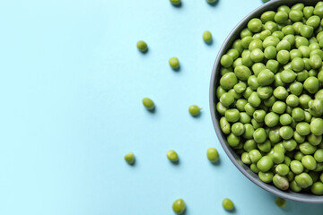 Bowl with fresh green peas on blue background