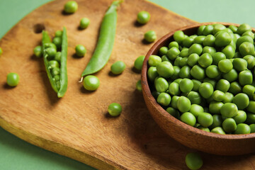Bowl and wooden board with fresh green peas on color background, closeup