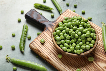 Bowl and wooden board with fresh green peas on grunge background