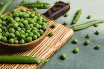 Bowl and wooden board with fresh green peas on grunge background