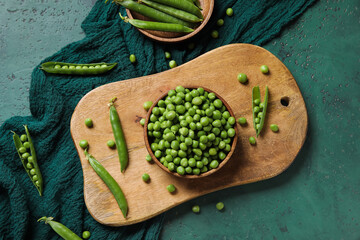 Bowls and wooden board with fresh green peas on color background
