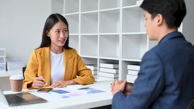 Two Asian business workers talking on the smartphone and using laptop at the office.