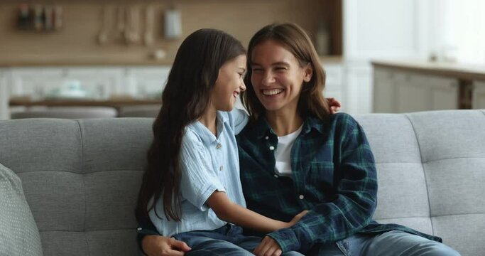 Happy loving mother hugging with affection little 10s daughter sit together on cozy sofa, discuss news, enjoy leisure time and good close relationship. Happy motherhood, communication, family ties