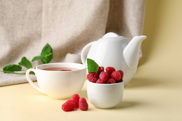 Bowl with fresh raspberries and cup of tea on yellow table