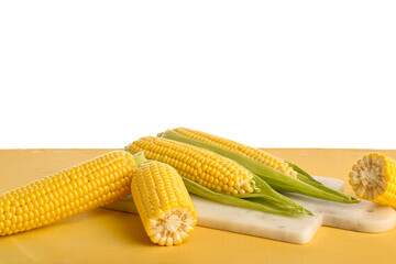 Board with fresh corn cobs on yellow table against white background