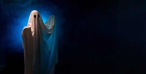 Spooky white ghost covered by a sheet with eyes stand over black background with smoke
