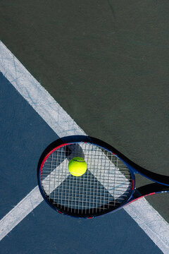 Overhead of tennis ball and tennis racket lying on tennis court on sunny day, copy space