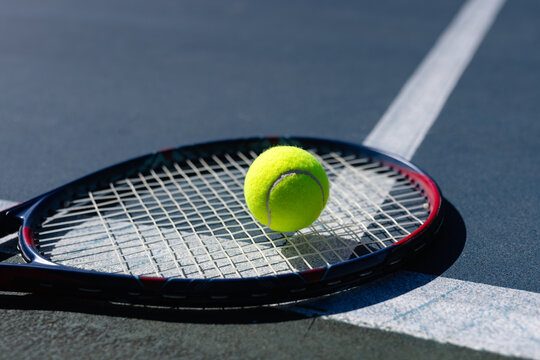 Close up of tennis ball and tennis racket lying on tennis court on sunny day, copy space