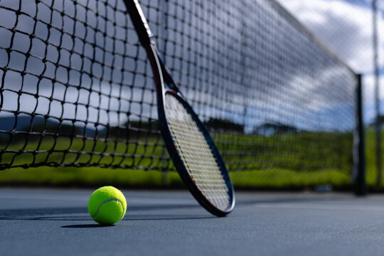 Close up of tennis ball and tennis racket against net on tennis court on sunny day, copy space