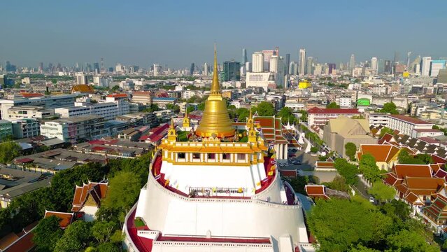 Aerial top view of Golden Mountain pagoda, a buddhist temple or Wat Saket in Bangkok Downtown, urban city with sunset sky, Thailand. Thai architecture landscape background.