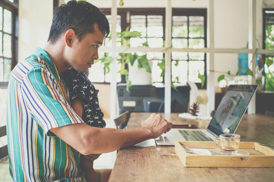 Asian daddy online working on laptop hold with toddler boy sitting in coffee shop
