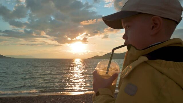 The boy drinking juice and looking on the sea. 4k slow motion footage UHD 3840x2160 