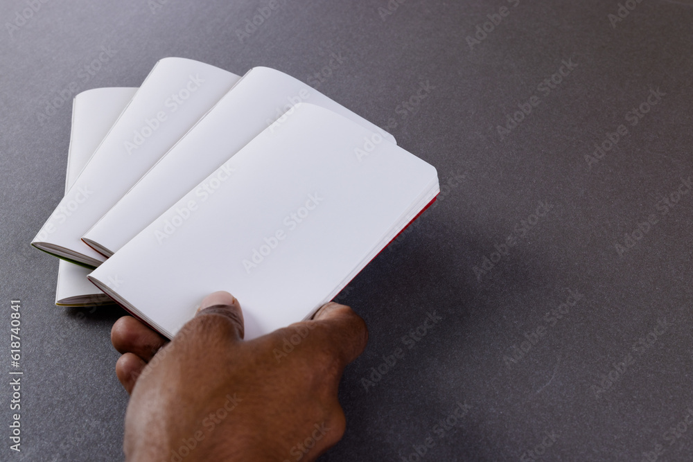 Poster hand of biracial man holding notebook over notebooks with copy space on grey background