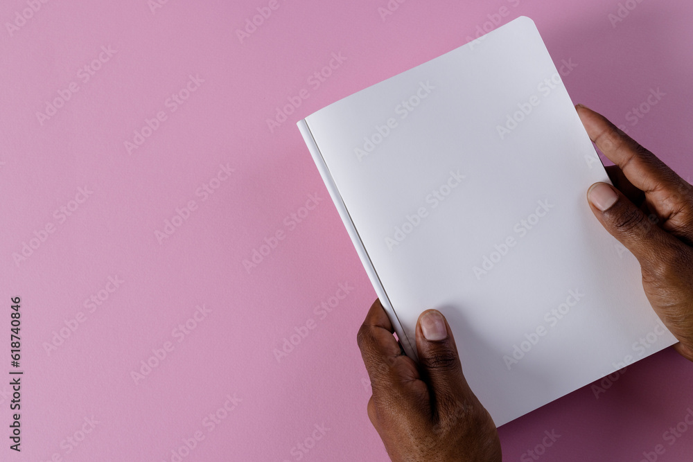 Poster Hands of biracial man holding book with copy space on pink background