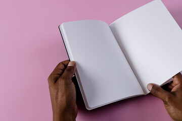Hands of biracial man holding book with copy space on pink background