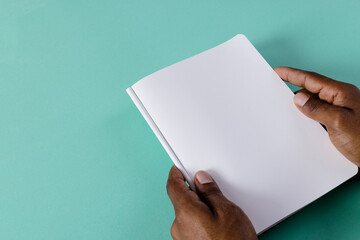 Hands of biracial man holding book with copy space on green background