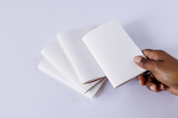 Hand of biracial man holding notebook over notebooks with copy space on white background