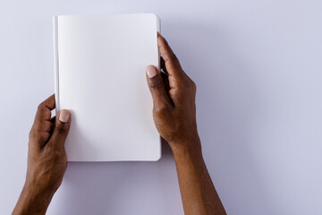 Hands of biracial man holding book with copy space on grey background