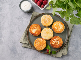 Pancakes with cottage cheese and fresh raspberry and sour cream on a light background with mint. The concept of a healthy and delicious morning breakfast.