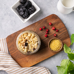 Millet porridge with prunes and fresh berry in a jar on a light background. The concept of a delicious, nutritious and healthy breakfast. Dietary and energy food.