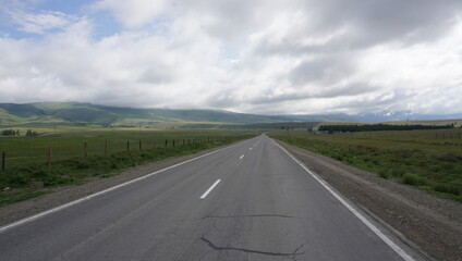Road through the steppe to the mountains with clouds