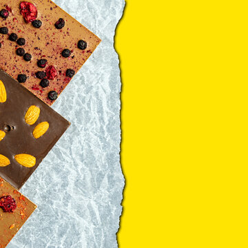 Chocolate bar with almonds, strawberries, raspberries and hazelnuts on a paper background. Sweetness with nuts. yellow space for inserting text. Square image.