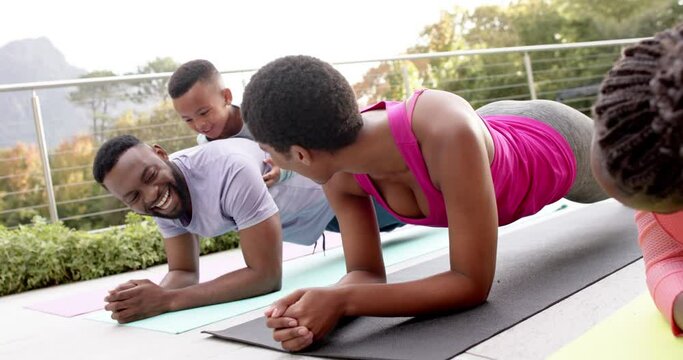 Happy african american parents, son and daughter practicing yoga in sunny garden, in slow motion