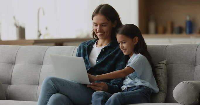 Happy young mother spend time with cute 10s daughter watch funny videos on-line on laptop, spend time on internet. Family leisure at home with modern wireless technology, electronic commerce clients