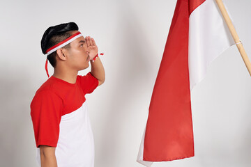 Young Asian man standing confidently looking at the Indonesian flag with giving a salute and...