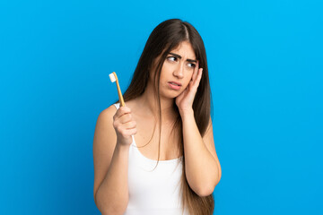 Young caucasian woman brushing teeth isolated on blue background with headache