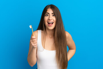 Young caucasian woman brushing teeth isolated on blue background with surprise facial expression
